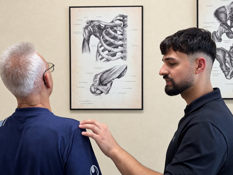 Jan-Dennis Pino Tellez bespricht mit einem Patienten den Befund vor einer anatomischen Zeichnung der Schulter