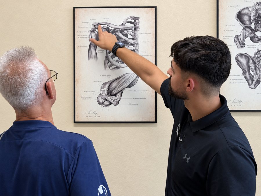 Jan-Dennis Pino Tellez erklärt einem Patienten an der anatomischen Zeichnung den Aufbau der Schulter