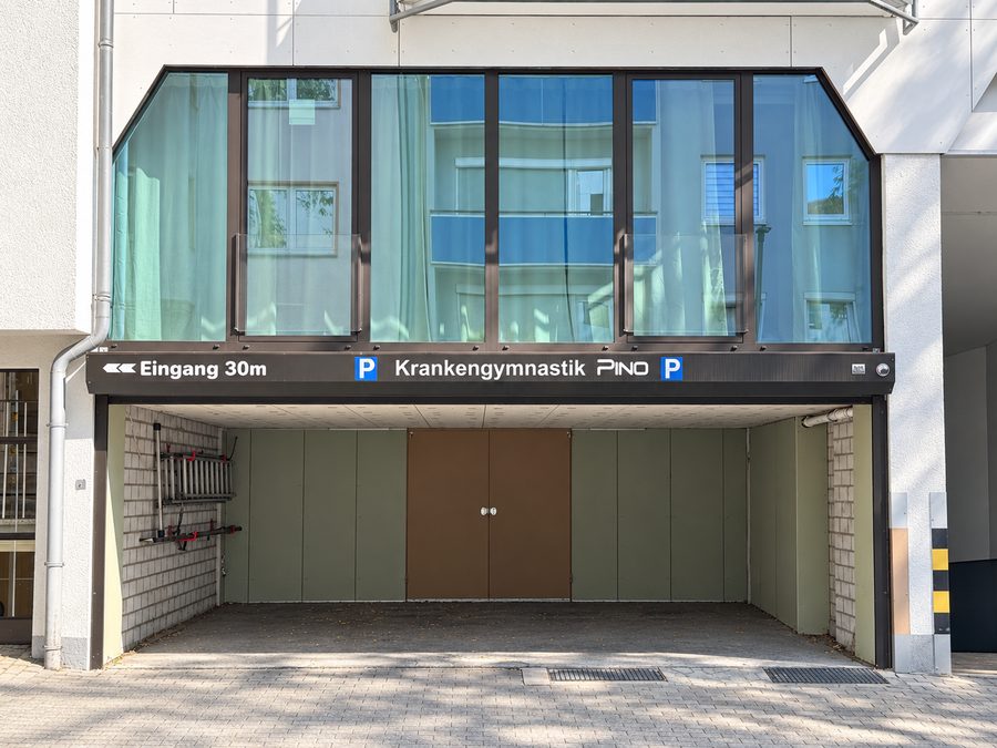 Einfahrt zu den Stellplätzen der Praxis mit dem Schild Krankengymnastik Pino, der Eingang liegt 30 Meter weiter